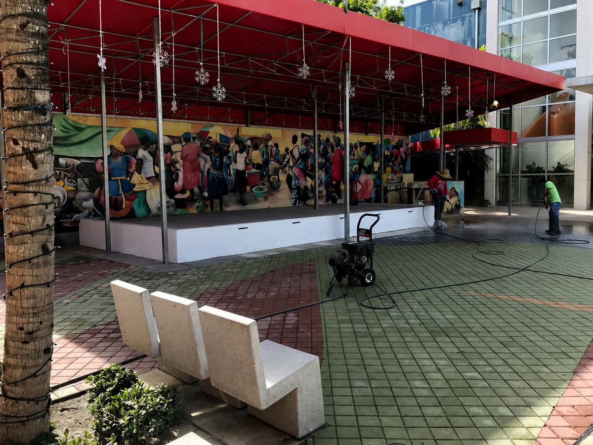 Completed red commercial canopy spanning the Haitian Cultural Center stage with hanging holiday decorations, mural and plaza pavers visible below.
