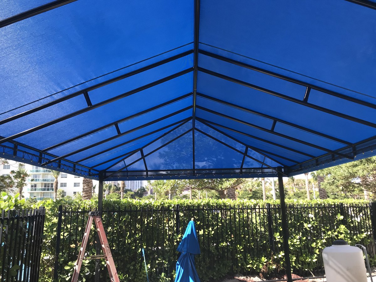 Underside of a hipped royal-blue fabric pavilion canopy on a black metal frame, looking up at the inside of the peaked roof against blue sky.
