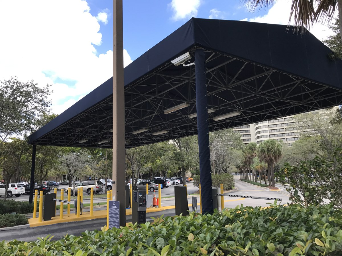 Dramatic upward angle of a navy hotel entry canopy showing exposed steel truss work supporting a clean tensioned fabric span.