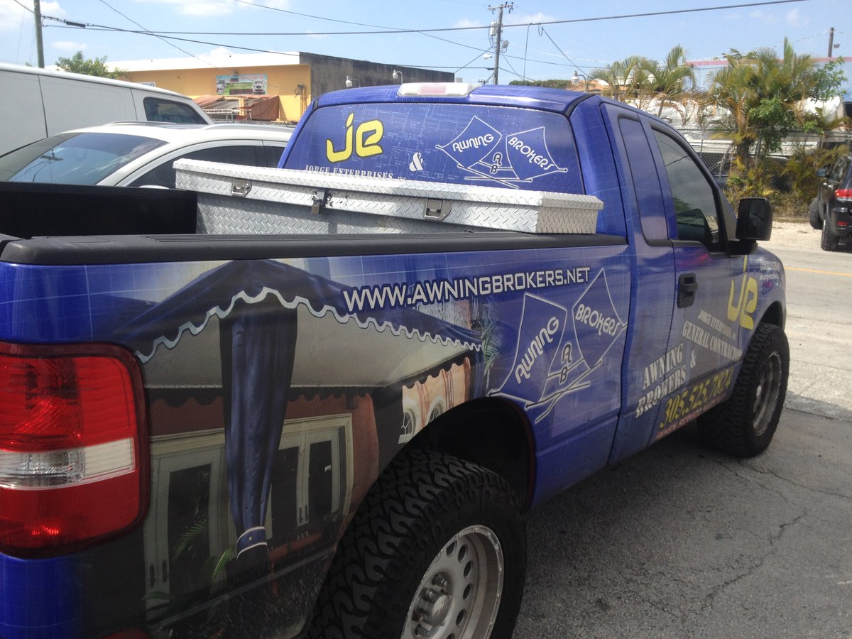 Side view of the JE Jorge Enterprises and Awning Brokers branded blue work truck with logo wrap and toolbox.