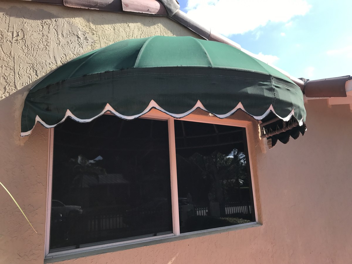 Forest-green dome window awning with scalloped white trim arches over a sliding glass window on a salmon stucco Mediterranean home with terra-cotta roof.