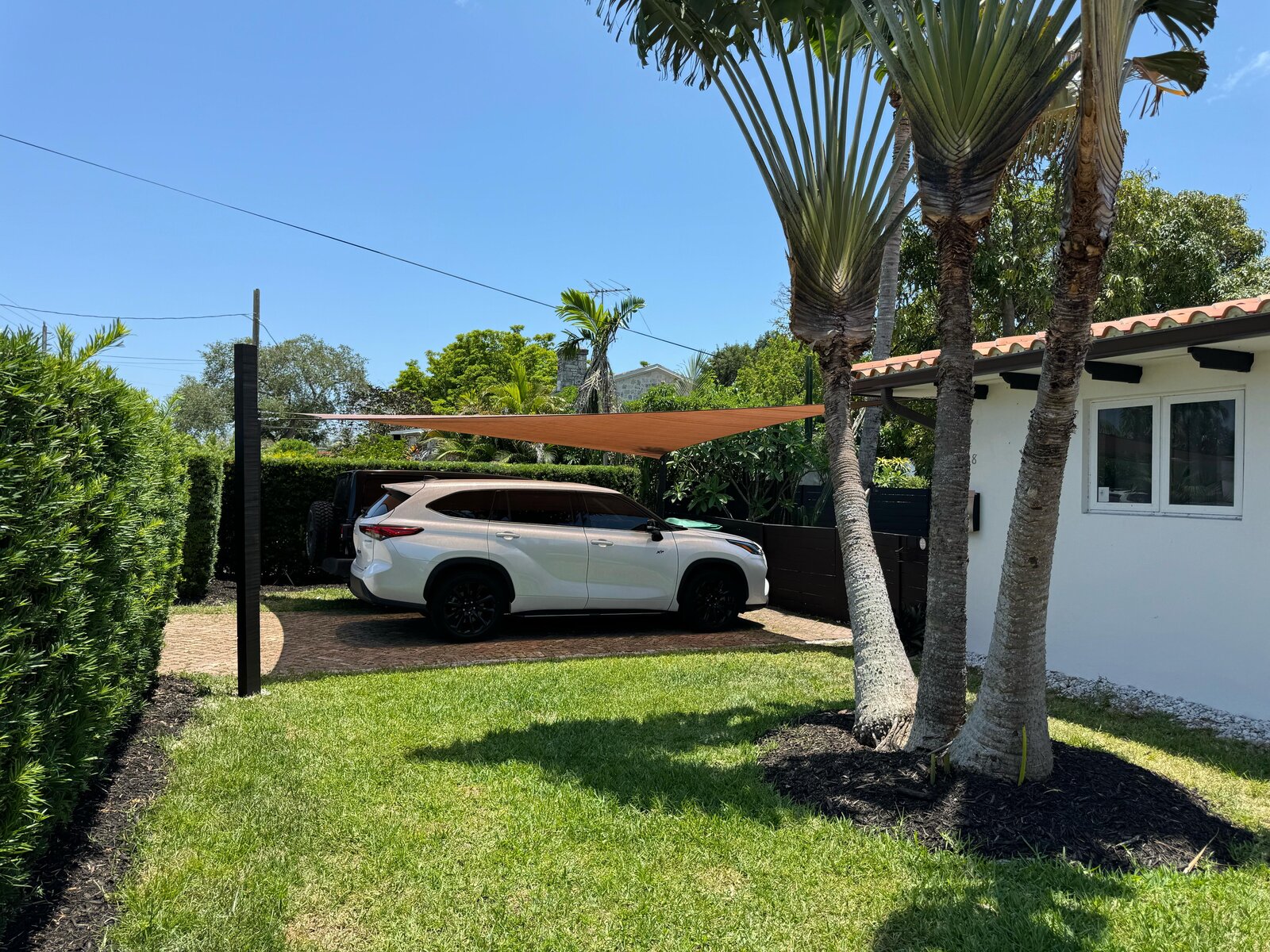 A custom tan fabric shade sail covering a white SUV in a South Florida driveway at dusk